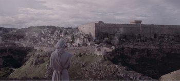 Movie still from “Mary Magdalene” (2018), directed by Garth Davis – A man in a hooded cloak standing in front of an old castle; Extreme Wide shot, High angle