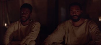 Movie still from “Mary Magdalene” (2018), directed by Garth Davis – A couple of men sitting next to each other in a dark room; Medium shot, Over the shoulder angle