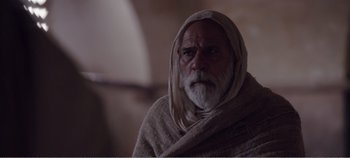 Movie still from “Mary Magdalene” (2018), directed by Garth Davis – An old man with a beard and a towel around his neck; Medium shot, Over the shoulder angle