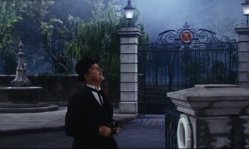 Movie still from “Mary Poppins” (1964), directed by Robert Stevenson – A man in a black suit and a black hat smoking a cigarette; Wide shot, Low angle