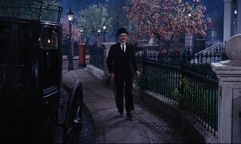 Movie still from “Mary Poppins” (1964), directed by Robert Stevenson – A man walking down a sidewalk next to an old fashioned car; Wide shot, Low angle
