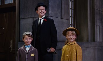 Movie still from “Mary Poppins” (1964), directed by Robert Stevenson – A man and two young children standing next to each other in front of a building; Medium shot, Low angle