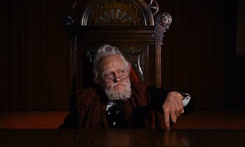 Movie still from “Mary Poppins” (1964), directed by Robert Stevenson – An old man sitting at a table in a chair; Medium shot, Low angle