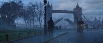Movie still from “Mary Poppins Returns” (2018), directed by Rob Marshall – A man is standing on the sidewalk in front of a bridge; Wide shot, Low angle