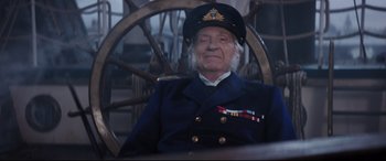 Movie still from “Mary Poppins Returns” (2018), directed by Rob Marshall – An older man in a uniform sitting in a chair; Medium shot, Over the shoulder angle
