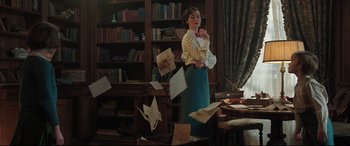 Movie still from “Mary Poppins Returns” (2018), directed by Rob Marshall – A woman standing in front of a bookshelf with papers flying in the air; Medium shot, Low angle