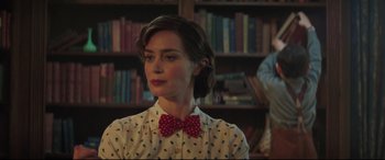 Movie still from “Mary Poppins Returns” (2018), directed by Rob Marshall – A woman with a red bow tie in a library; Close Up shot, Over the shoulder angle