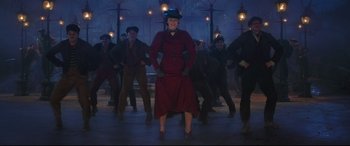 Movie still from “Mary Poppins Returns” (2018), directed by Rob Marshall – A group of men and women dancing in front of lights; Wide shot, Low angle