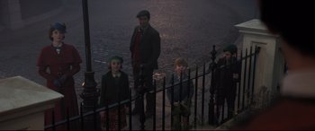 Movie still from “Mary Poppins Returns” (2018), directed by Rob Marshall – A man and two children standing next to a fence; Wide shot, High angle