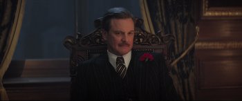 Movie still from “Mary Poppins Returns” (2018), directed by Rob Marshall – A man in a suit and tie sitting in a chair; Close Up shot, Low angle