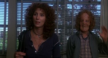 Movie still from “Mask” (1985), directed by Peter Bogdanovich – A woman and a man standing next to each other in a room; Close Up shot, Low angle