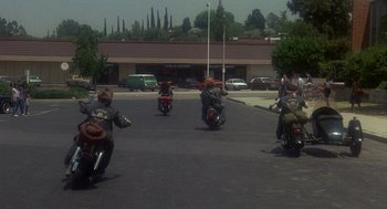 Movie still from “Mask” (1985), directed by Peter Bogdanovich – A group of people riding motorcycles down a street; Wide shot, High angle