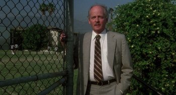 Movie still from “Mask” (1985), directed by Peter Bogdanovich – A man in a suit and tie leaning against a fence; Medium shot, Low angle