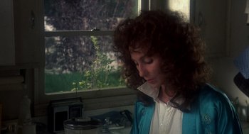Movie still from “Mask” (1985), directed by Peter Bogdanovich – A person sitting at a table near a window; Close Up shot, Over the shoulder angle