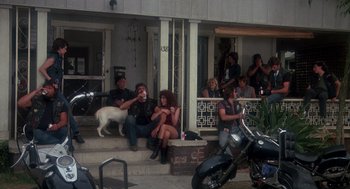 Movie still from “Mask” (1985), directed by Peter Bogdanovich – A group of people sitting on the steps of a house with a dog; Wide shot, High angle