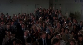 Movie still from “Mask” (1985), directed by Peter Bogdanovich – A large group of people sitting in a room; Wide shot, High angle