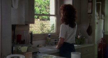 Movie still from “Mask” (1985), directed by Peter Bogdanovich – A woman standing at a sink looking out a window; Medium shot, High angle