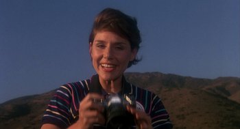Movie still from “Mask” (1985), directed by Peter Bogdanovich – A woman holding a camera in front of a mountain; Close Up shot, Low angle