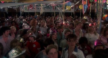 Movie still from “Mask” (1985), directed by Peter Bogdanovich – A crowd of people sitting and standing in front of a birthday sign; Wide shot, High angle