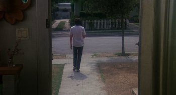 Movie still from “Mask” (1985), directed by Peter Bogdanovich – A man walking down a sidewalk near a tree; Wide shot, High angle