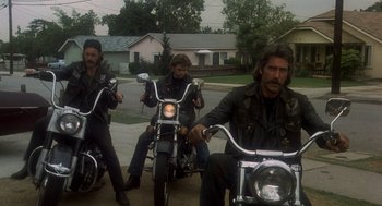 Movie still from “Mask” (1985), directed by Peter Bogdanovich – A group of men riding motorcycles down a street; Medium shot, Low angle