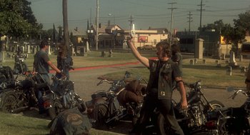Movie still from “Mask” (1985), directed by Peter Bogdanovich – A group of people standing next to motorcycles on the side of the road; Wide shot, Low angle