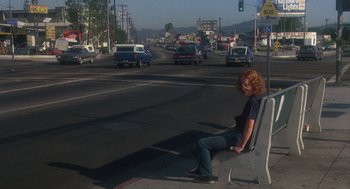 Movie still from “Mask” (1985), directed by Peter Bogdanovich – A person sitting on a bench on the side of the road; Wide shot, High angle