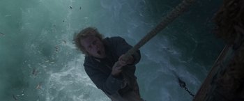 Movie still from “Master and Commander: The Far Side of the World” (2003), directed by Peter Weir – A man holding on to a rope in front of the ocean; Medium shot, Overhead angle