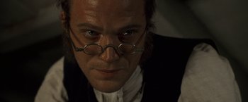 Movie still from “Master and Commander: The Far Side of the World” (2003), directed by Peter Weir – A person wearing glasses and a suit; Close Up shot, Over the shoulder angle