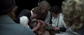 Movie still from “Master and Commander: The Far Side of the World” (2003), directed by Peter Weir – A group of people are gathered around a man's face; Medium shot, Over the shoulder angle