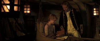 Movie still from “Master and Commander: The Far Side of the World” (2003), directed by Peter Weir – A young man sitting next to an older man reading a book; Medium shot, High angle