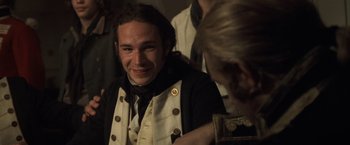 Movie still from “Master and Commander: The Far Side of the World” (2003), directed by Peter Weir – A man in a vest is smiling for the camera; Close Up shot, Over the shoulder angle
