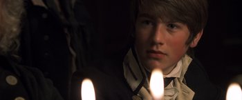 Movie still from “Master and Commander: The Far Side of the World” (2003), directed by Peter Weir – A young man is holding two lit candles in front of his face; Close Up shot, Over the shoulder angle