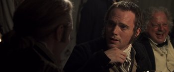 Movie still from “Master and Commander: The Far Side of the World” (2003), directed by Peter Weir – A man sitting next to another man in front of a wall; Close Up shot, Over the shoulder angle