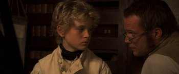 Movie still from “Master and Commander: The Far Side of the World” (2003), directed by Peter Weir – A young boy wearing a white shirt and a black bow tie; Close Up shot, Over the shoulder angle