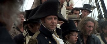 Movie still from “Master and Commander: The Far Side of the World” (2003), directed by Peter Weir – A group of people in a crowd wearing hats; Close Up shot, Over the shoulder angle
