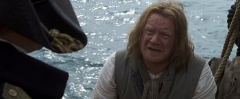 Movie still from “Master and Commander: The Far Side of the World” (2003), directed by Peter Weir – A man with long blonde hair is standing in the water; Close Up shot, Over the shoulder angle