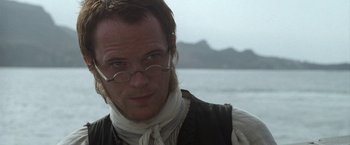 Movie still from “Master and Commander: The Far Side of the World” (2003), directed by Peter Weir – A person wearing glasses and a vest; Close Up shot, Over the shoulder angle