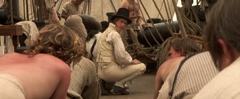 Movie still from “Master and Commander: The Far Side of the World” (2003), directed by Peter Weir – A man sitting on the floor of a ship; Medium shot, Over the shoulder angle