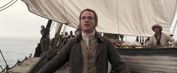 Movie still from “Master and Commander: The Far Side of the World” (2003), directed by Peter Weir – A man standing in front of a group of people on a boat; Medium shot, High angle