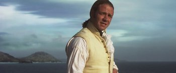 Movie still from “Master and Commander: The Far Side of the World” (2003), directed by Peter Weir – A man in a white shirt and a yellow vest standing in front of a body of water; Close Up shot, Over the shoulder angle
