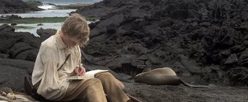 Movie still from “Master and Commander: The Far Side of the World” (2003), directed by Peter Weir – A man sitting on the ground writing in a notebook; Medium shot, High angle