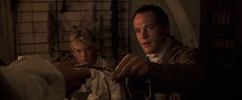 Movie still from “Master and Commander: The Far Side of the World” (2003), directed by Peter Weir – Two men sitting at a dinner table with a knife and a fork; Close Up shot, Over the shoulder angle