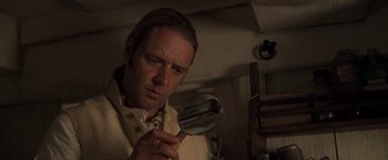 Movie still from “Master and Commander: The Far Side of the World” (2003), directed by Peter Weir – A man holding a mirror in a room; Close Up shot, Over the shoulder angle