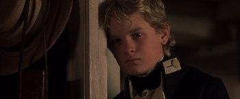 Movie still from “Master and Commander: The Far Side of the World” (2003), directed by Peter Weir – A young boy wearing a suit and tie looking at the camera; Close Up shot, High angle