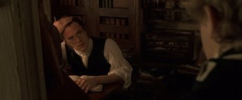 Movie still from “Master and Commander: The Far Side of the World” (2003), directed by Peter Weir – A man sitting at a table in front of books; Medium shot, High angle
