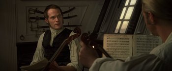 Movie still from “Master and Commander: The Far Side of the World” (2003), directed by Peter Weir – A man holding a violin and a cello; Close Up shot, Over the shoulder angle
