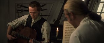 Movie still from “Master and Commander: The Far Side of the World” (2003), directed by Peter Weir – A man playing a violin in front of a candle; Medium shot, Over the shoulder angle