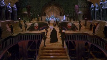 Movie still from “Masters of the Universe” (1987), directed by Gary Goddard – A group of people standing in a room with stairs leading up to them; Extreme Wide shot, High angle