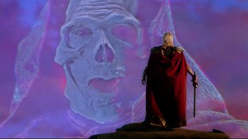 Movie still from “Masters of the Universe” (1987), directed by Gary Goddard – A man in a red cloak standing in front of a painting of a face; Medium shot, Over the shoulder angle